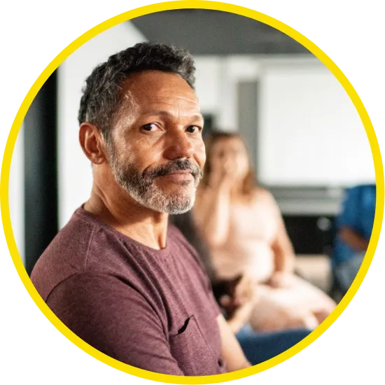 Man with salt-and-pepper beard looking at the camera while attending a support group session