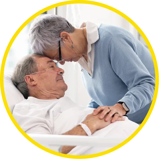 Elderly woman gently leaning her forehead against a hospitalized man's as he lies in bed with an oxygen tube