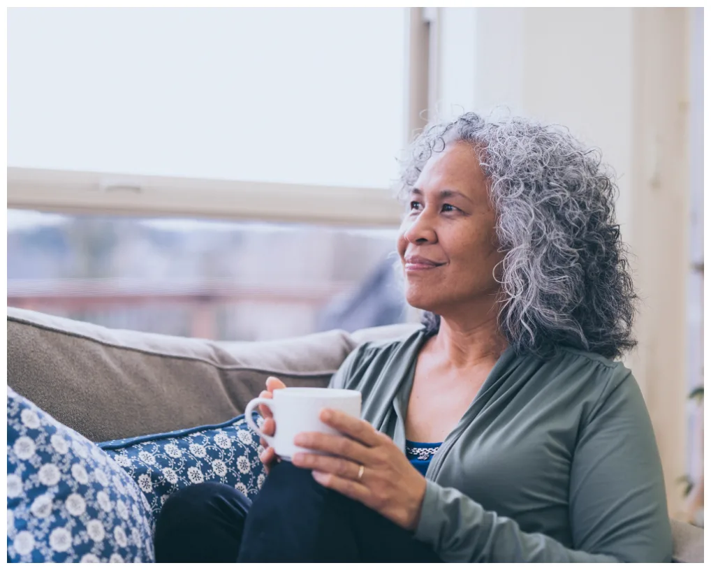 woman smiling holding a mug while looking out the window